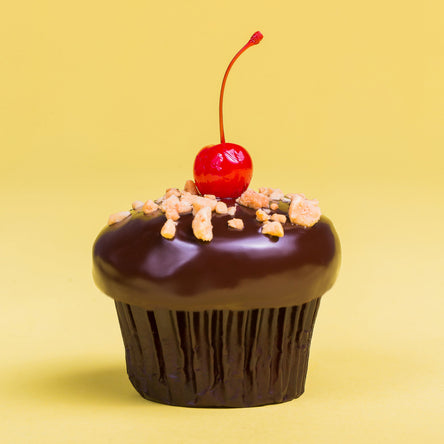 banana split cupcake with banana cake, marshmallow filling, and strawberry frosting, that has been dipped in ganache and finished with crushed peanuts and a maraschino cherry