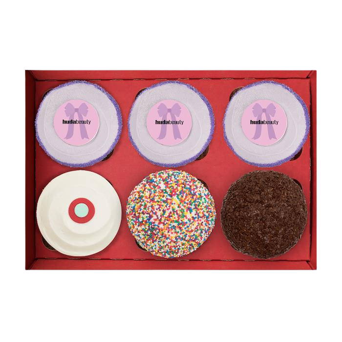 Top view of Huda Beauty 6 box with 3 Huda Beauty Ube Birthday Cupcakes, 1 red velvet, 1 sprinkle, and 1 dark chocolate cupcake. not-bg