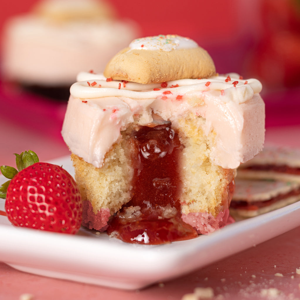 pop tart cupcake with a pink sugar cookie crust, strawberry jam filling, all topped with strawberry frosting and finished with drizzled vanilla buttercream, red sugar crystals and a mini pop tart