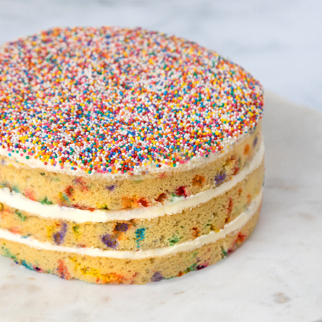 three tiered Sprinkle layer cake topped with rainbow sprinkles